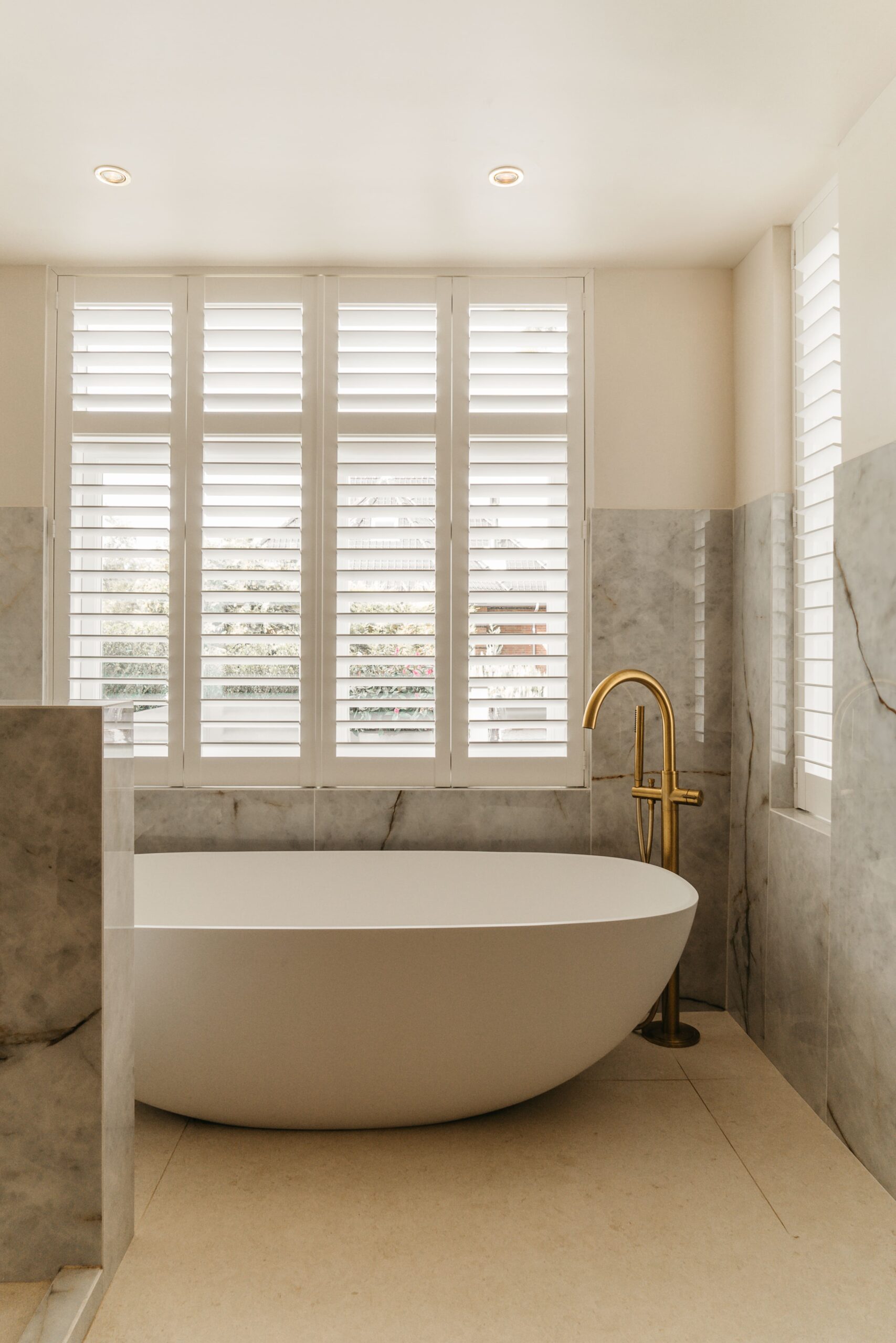 Vrijstaand mat wit JEE-O ligbad met geborsteld gouden vrijstaande badkraan in luxe badkamer met Himalaya Crystal marmerlook tegels
